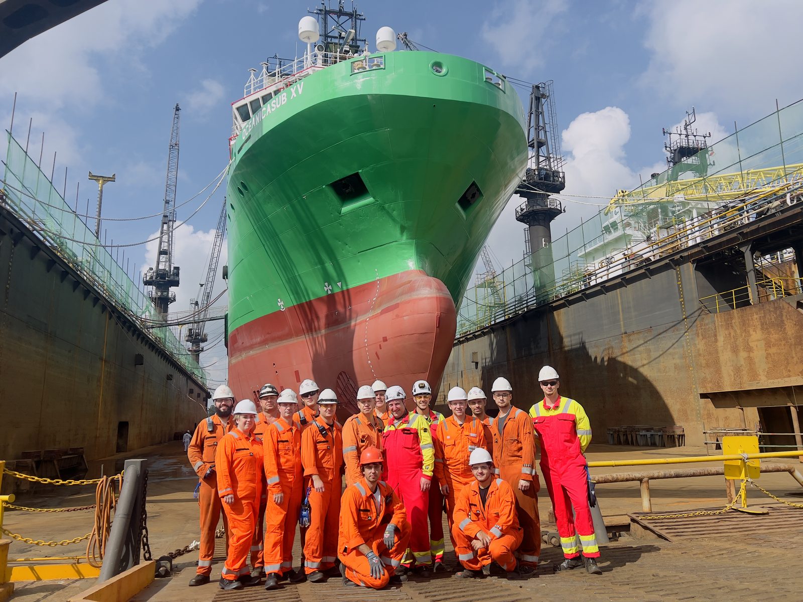 Crew and yard team posing in dry dock in front of the newly painted green bow of Oceanicasub XV.