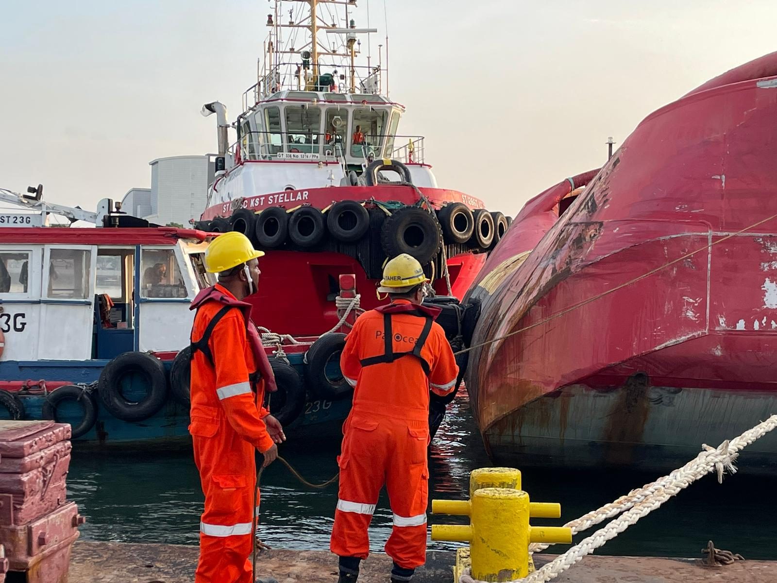 Harbor tug KST Stellar assisting alongside during a docking or towage manoeuvre, crew handling mooring lines in the foreground