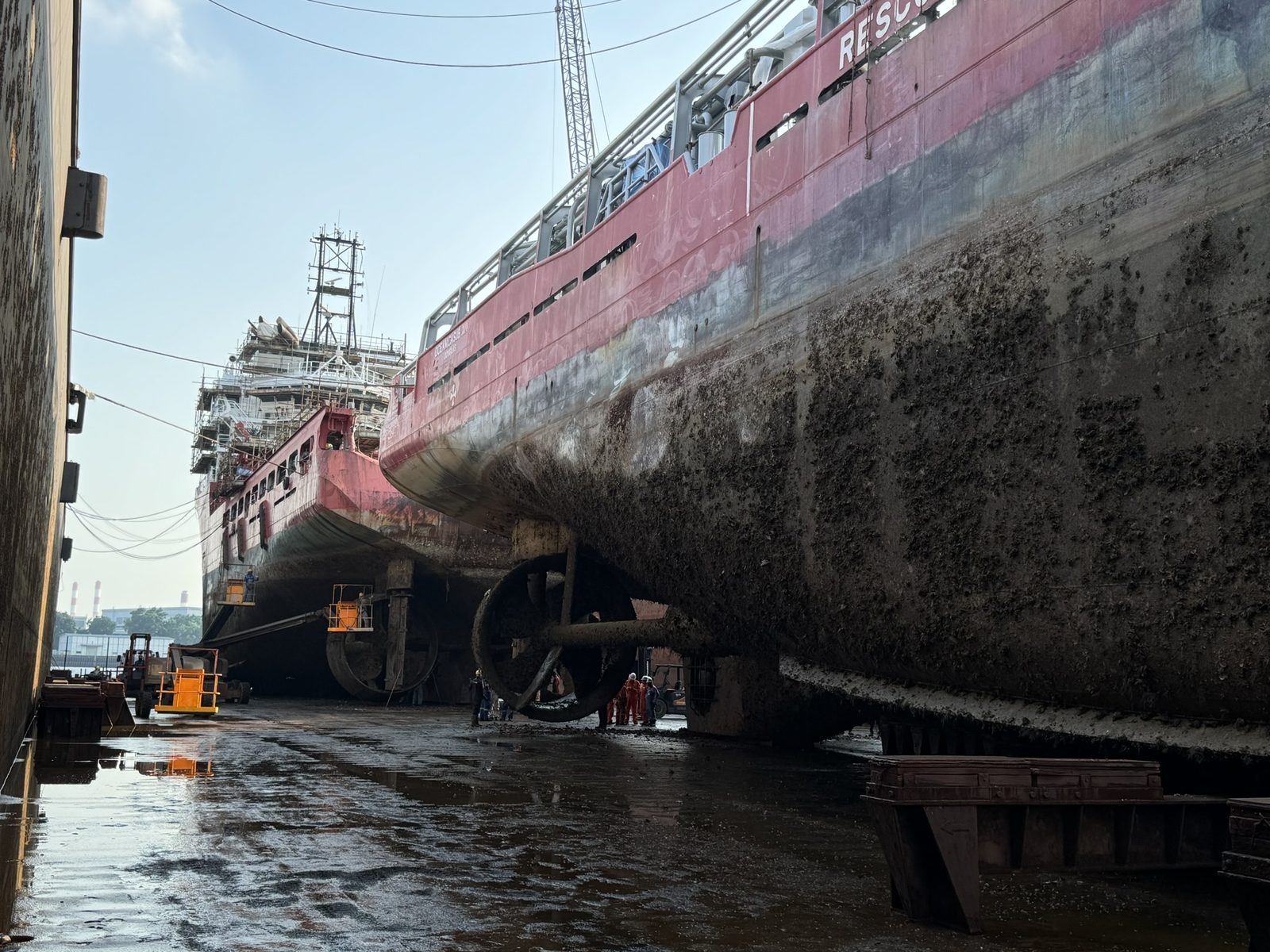 Two AHTS sister vessels in dry dock in Singapore; the background hull reads Oceanicasub XIV, heavily fouled below the waterline from her laid-up period.