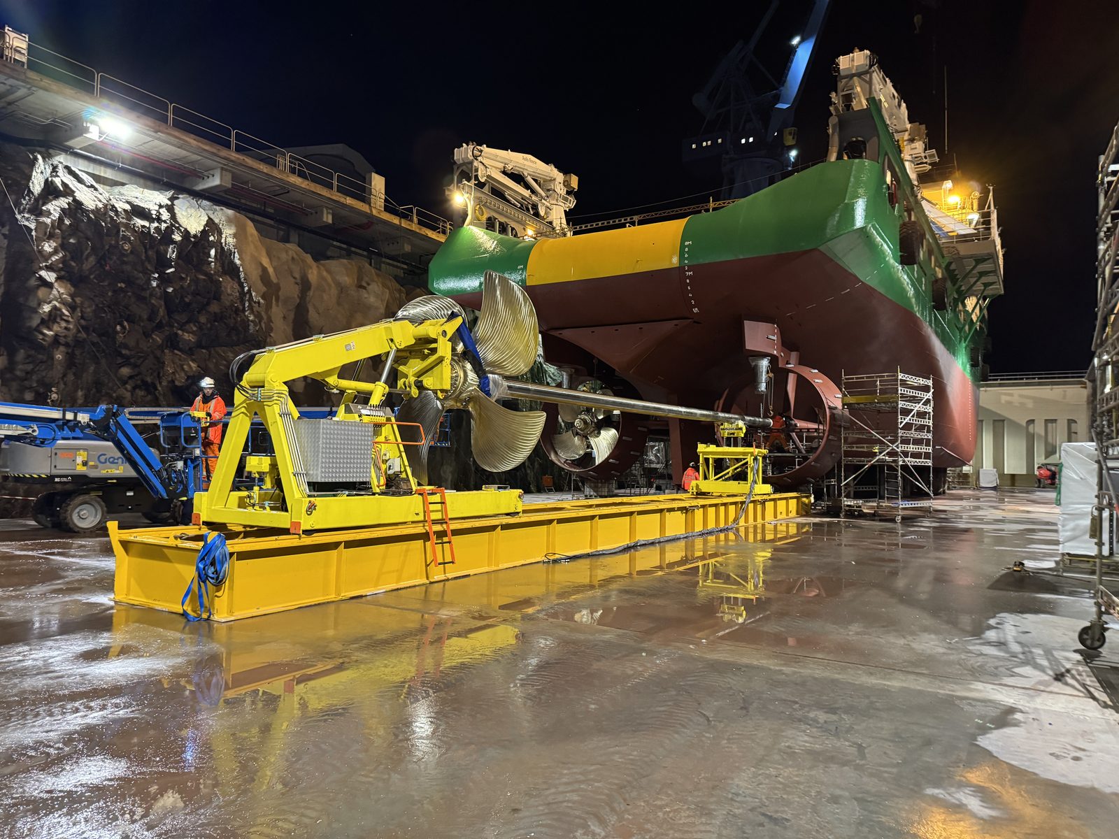 A ship's propeller and thruster assembly on a service platform beside Oceanicasub XVII's hull during night-shift dry dock work