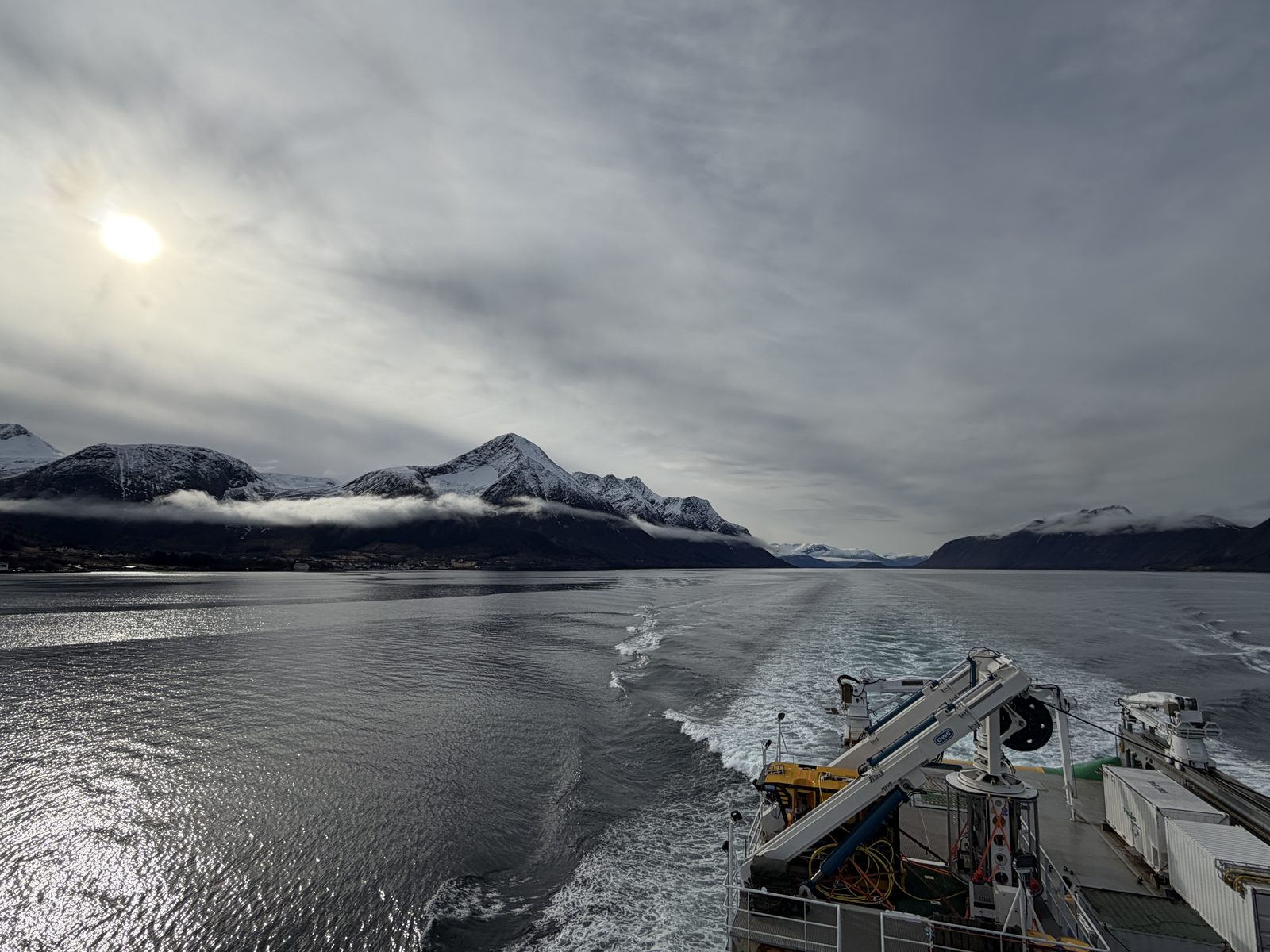 View from Oceanicasub XVII's stern crossing a Norwegian fjord under snow-capped mountains, the ROV handling crane visible on deck, departing for Brazil.