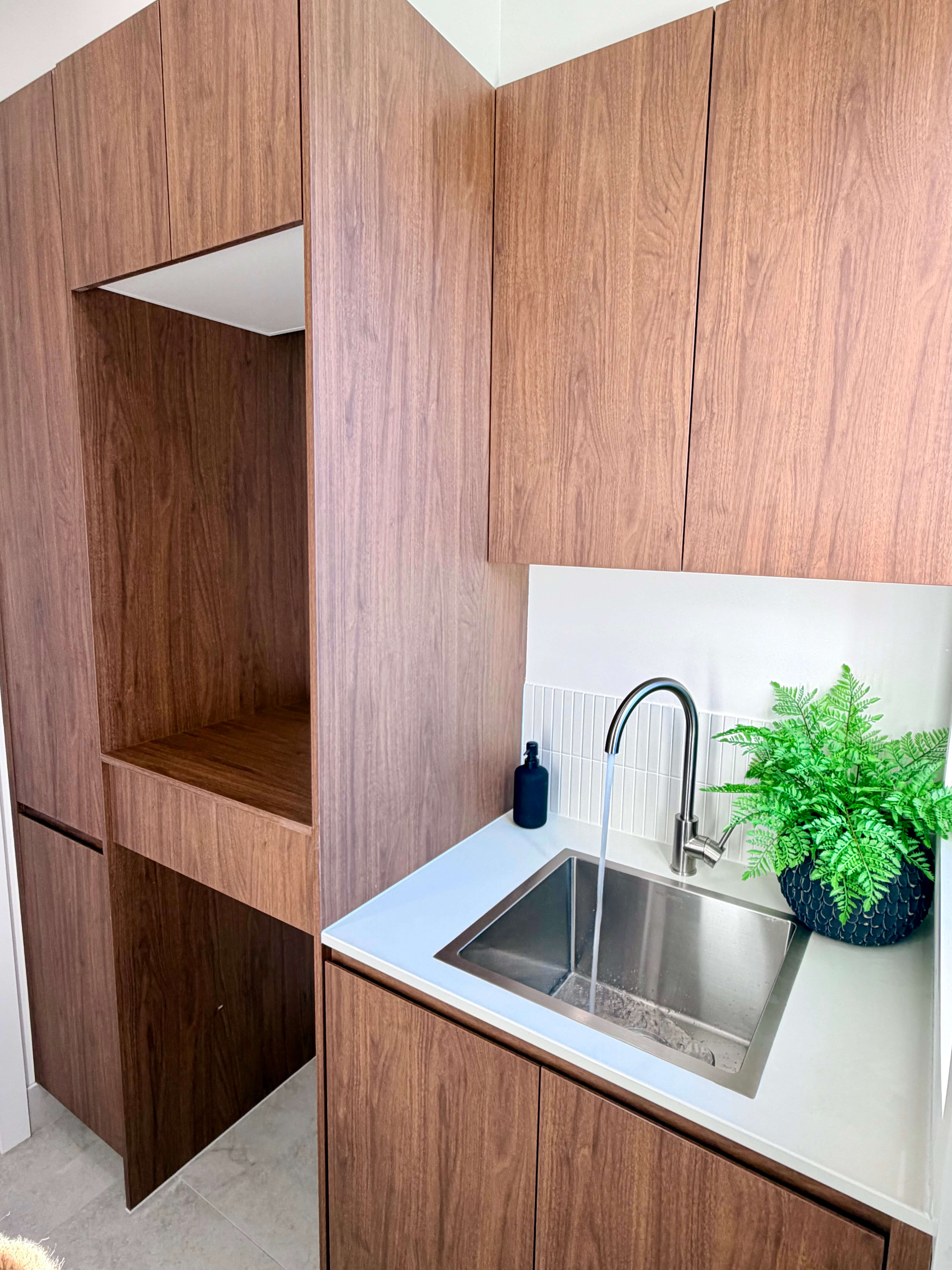 Custom laundry with dark walnut cabinetry, natural stone benchtops and bespoke joinery, expertly crafted for style and functionality.