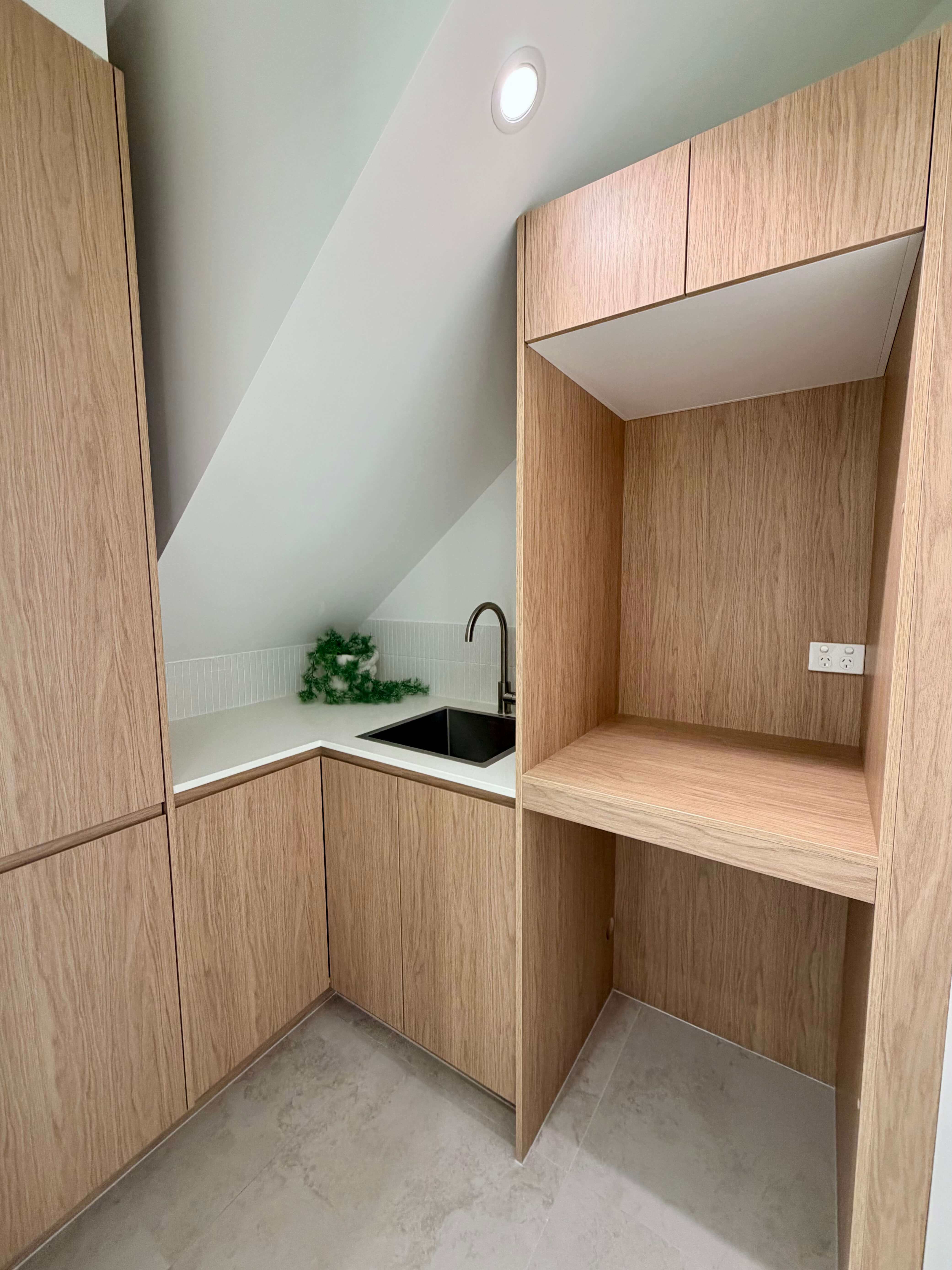 Compact under-stair laundry with bright custom cabinetry, natural stone benchtops and bespoke joinery.