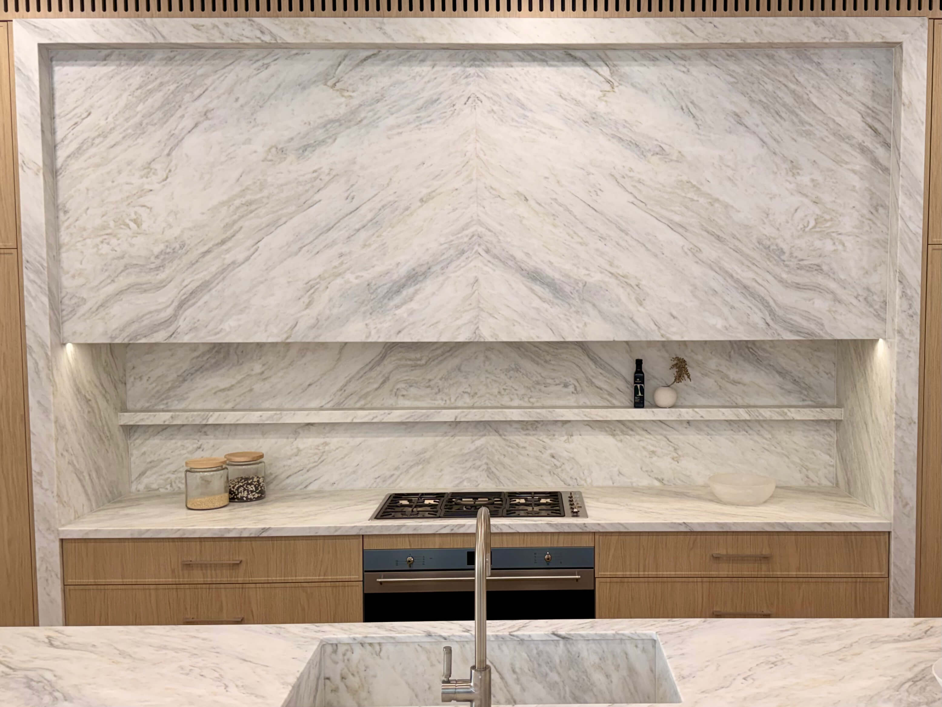 Spacious open-plan kitchen featuring natural stone benchtops, bright custom joinery and timeless luxury finishes.