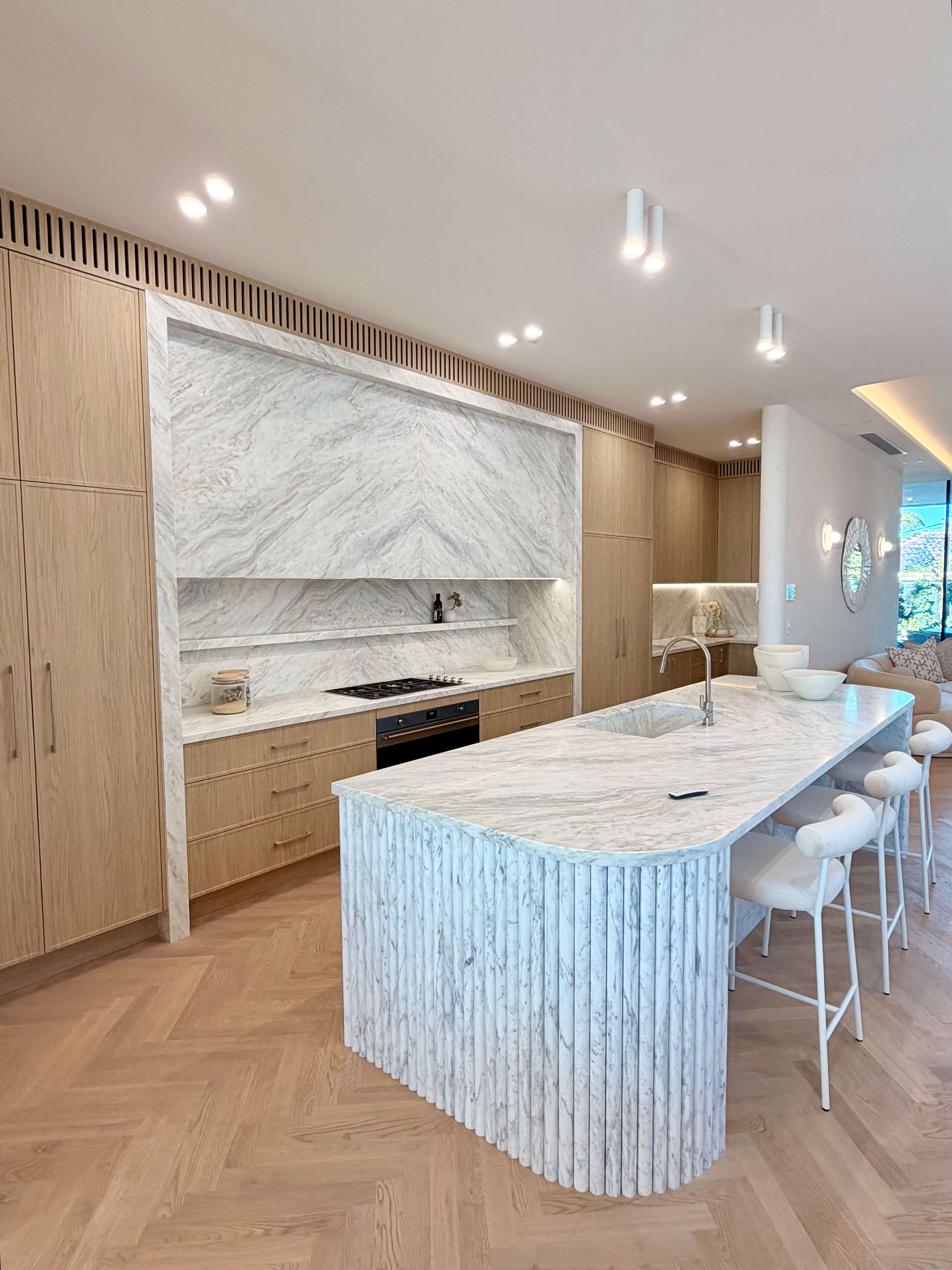 Luxury kitchen featuring a custom marble fluted island, bright natural stone and premium bespoke cabinetry.