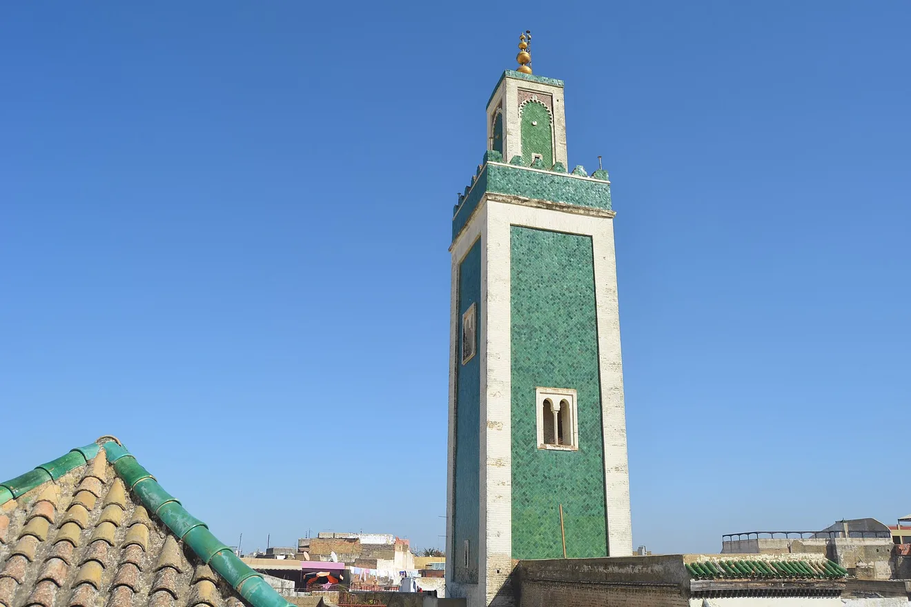 A minaret clad in green ceramic tiles rises above the rooftops of the Meknes medina.