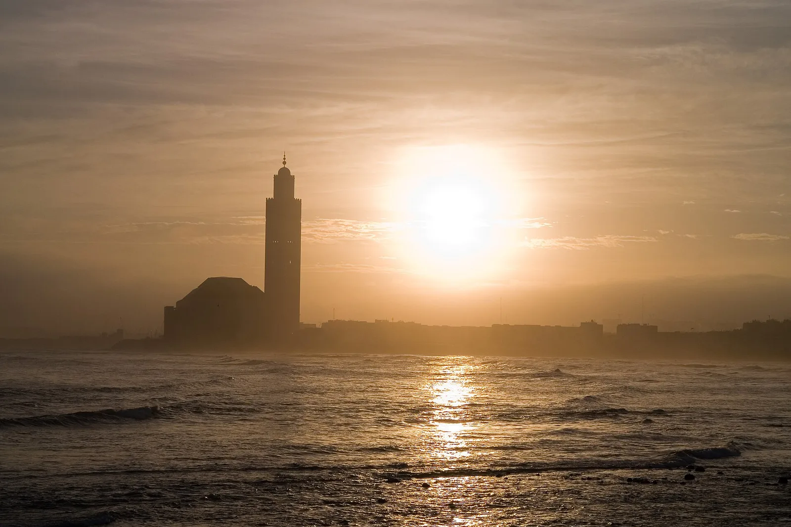 The Hassan II Mosque in Casablanca against the light, with the sun low over the Atlantic Ocean.