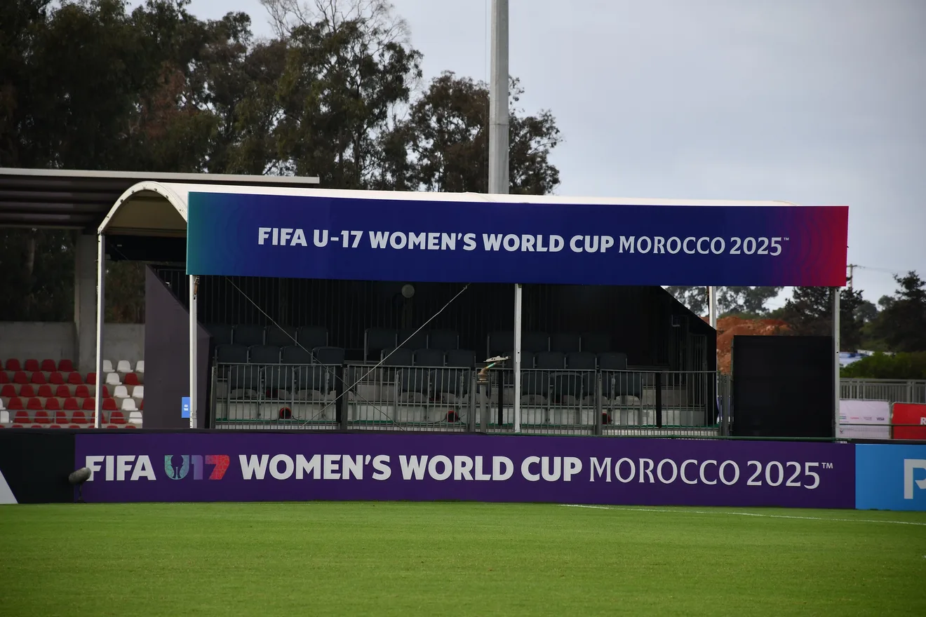 The stand at the Mohammed VI Football Complex in Sale, dressed in the colors of the 2025 U17 Women’s World Cup in Morocco, facing an empty pitch under a gray sky.