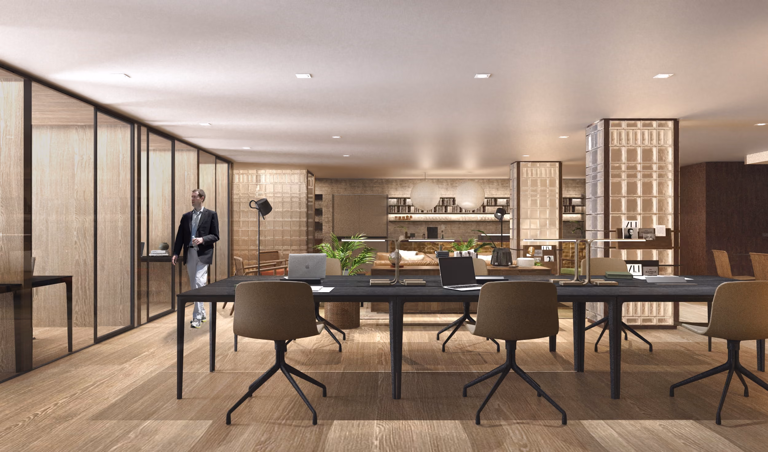 Modern office space with a long black table, brown swivel chairs, laptops, and a man walking near glass-walled meeting rooms.