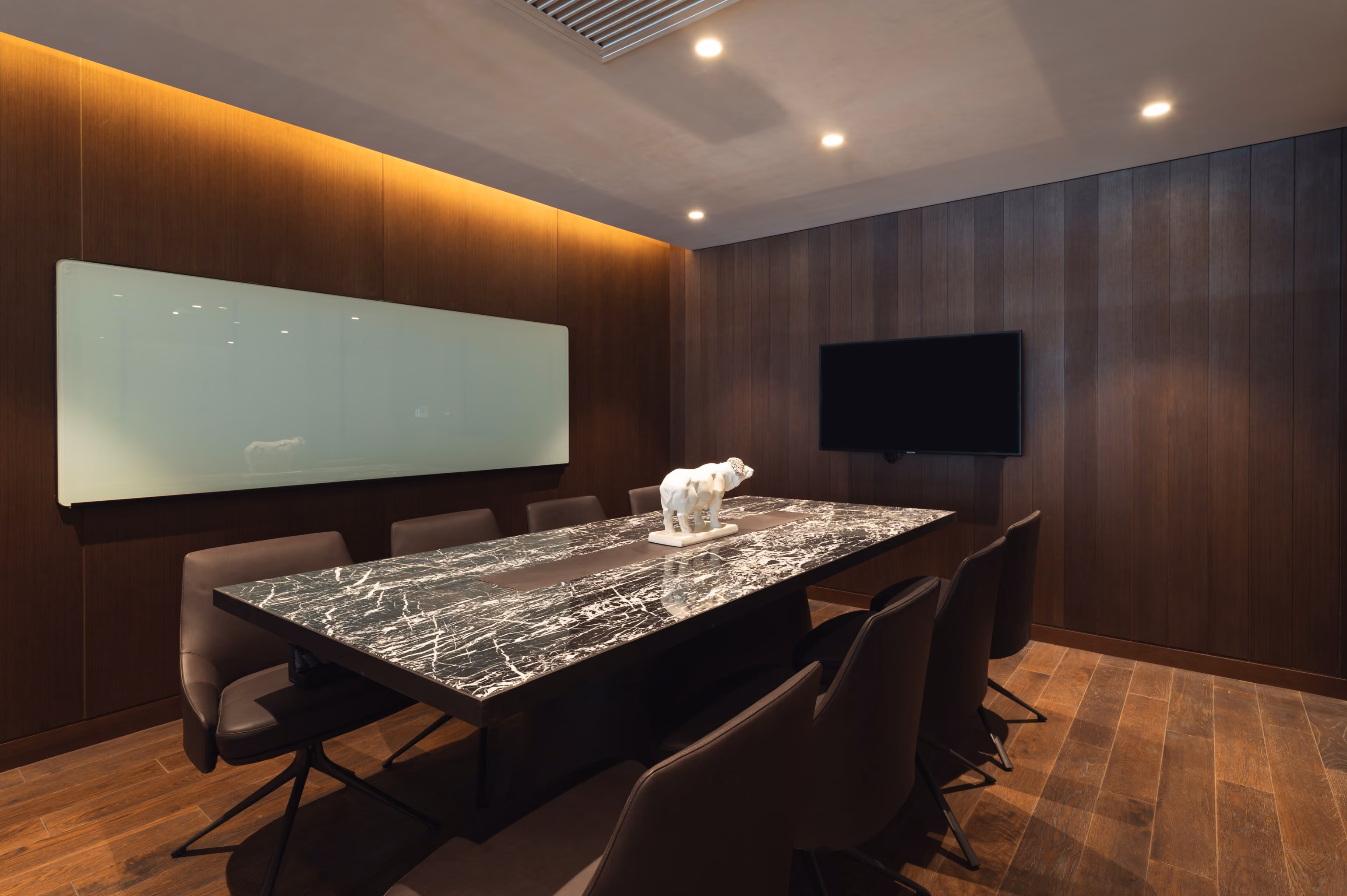 Conference room with a black marble table, six brown chairs, whiteboard, TV, and a white elephant statue.