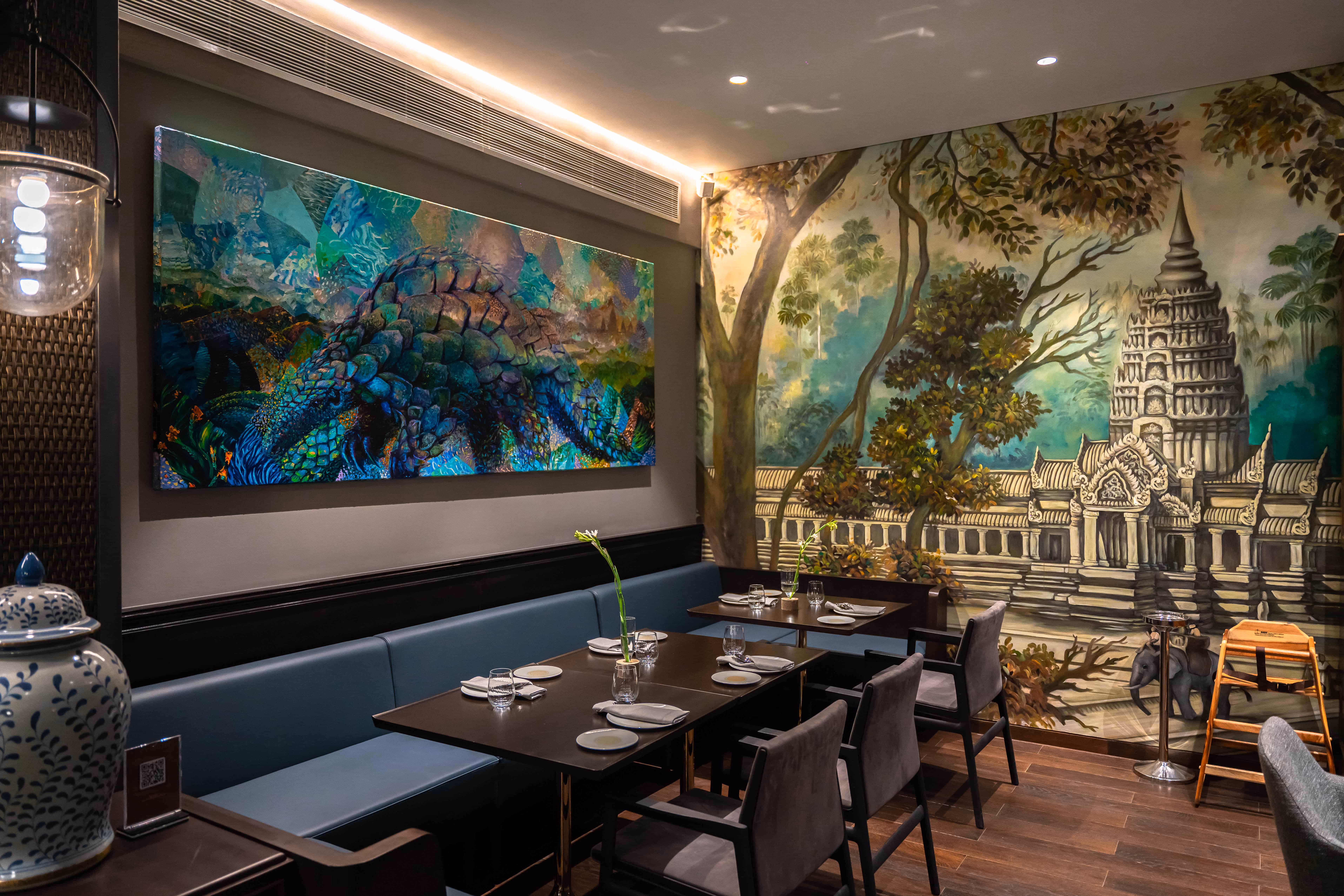 Interior of a restaurant with blue seating, dark tables, a reptile painting, and a mural of a temple and trees.