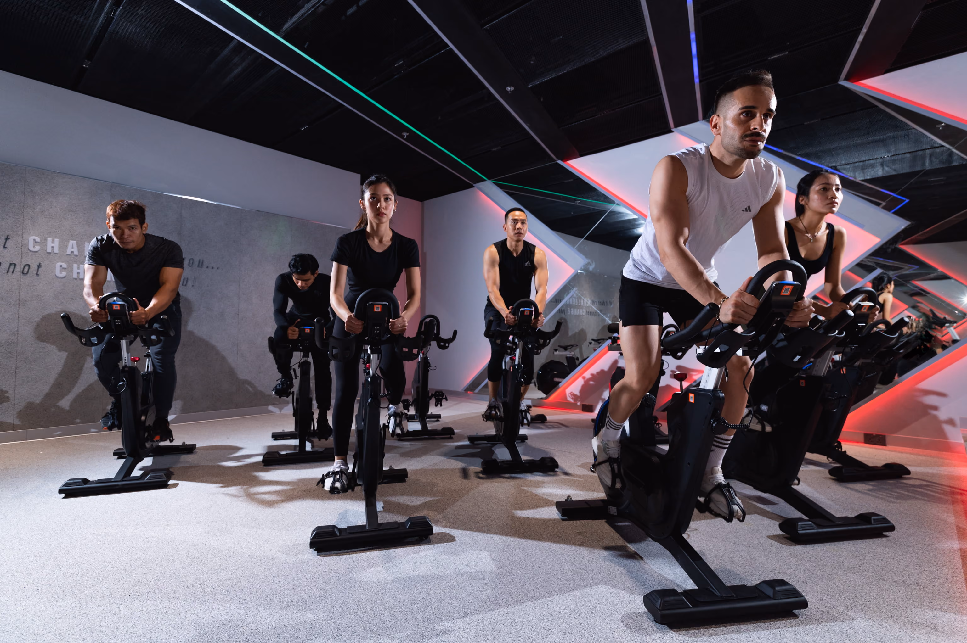 Group of six people intensely cycling on stationary bikes in a modern gym spin class.
