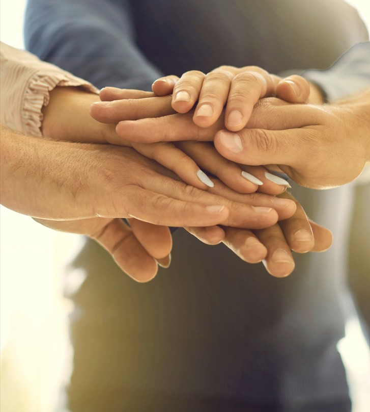 Meerdere handen op elkaar gestapeld, symboliseert samenwerking en eenheid.