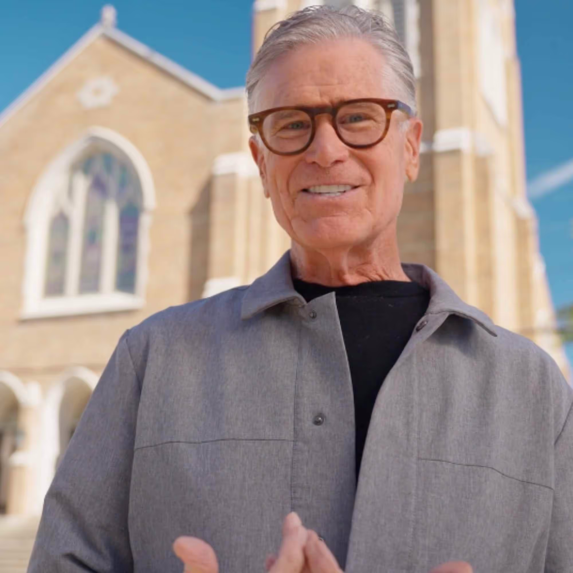 Emerson Eggerichs, PhD smiling with glasses and gray hair wearing a gray jacket, standing outdoors in front of a church building.