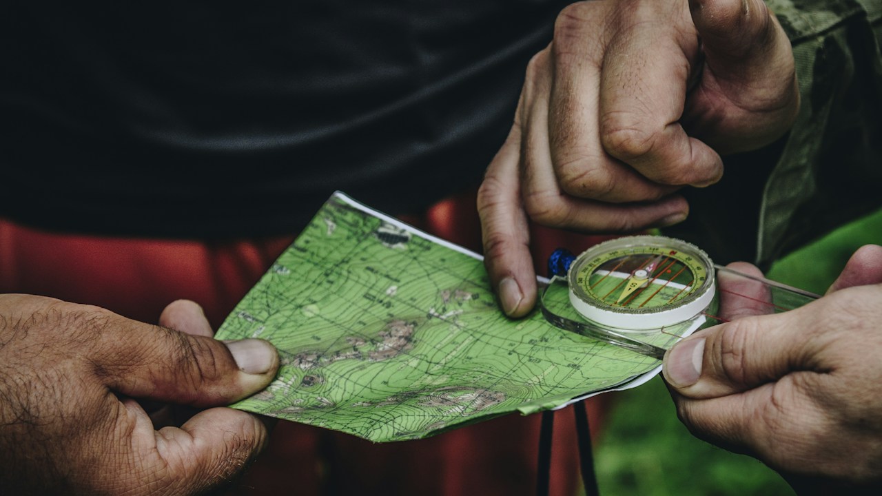 Two people's hands holding a map and compass, working out which direction to go