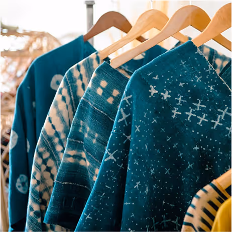 Close-up of blue and teal patterned sweaters hanging on wooden hangers in a clothing store.