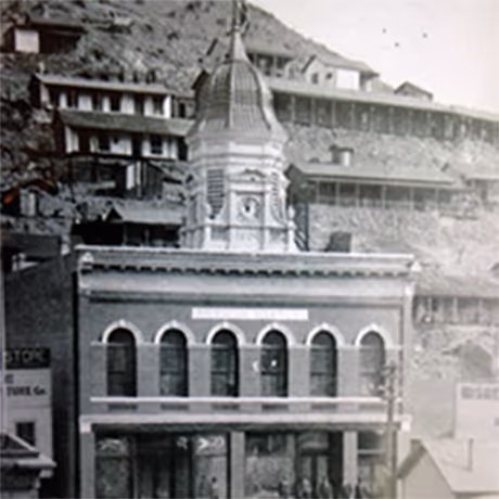 Historic black-and-white photo of a two-story building with arched windows and a prominent clock tower with a dome on top.