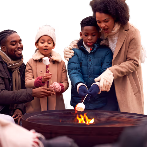 Family gathered around a firepit roasting marshmallows during a community evening event.