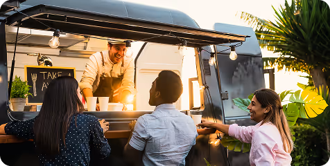 Three people ordering drinks at a food truck served by a smiling vendor in an apron.