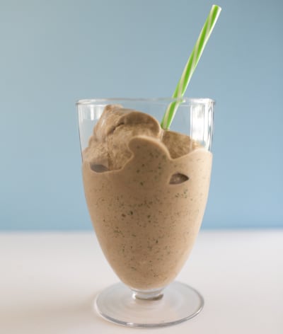 A healthy looking chocolate shake with a green and white straw