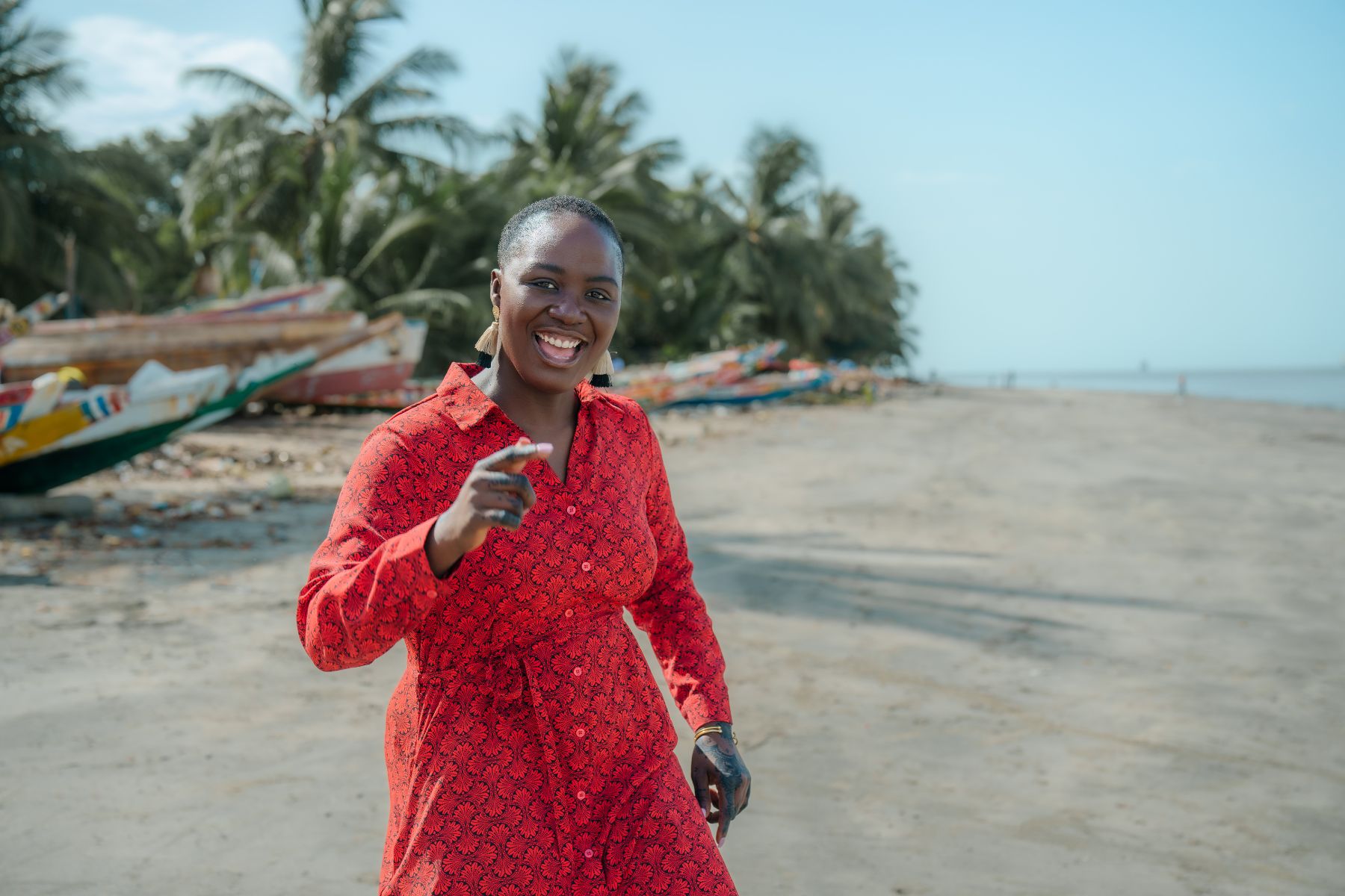 Pelumi Nubi in a red dress on a beach, wooden boats behind her.