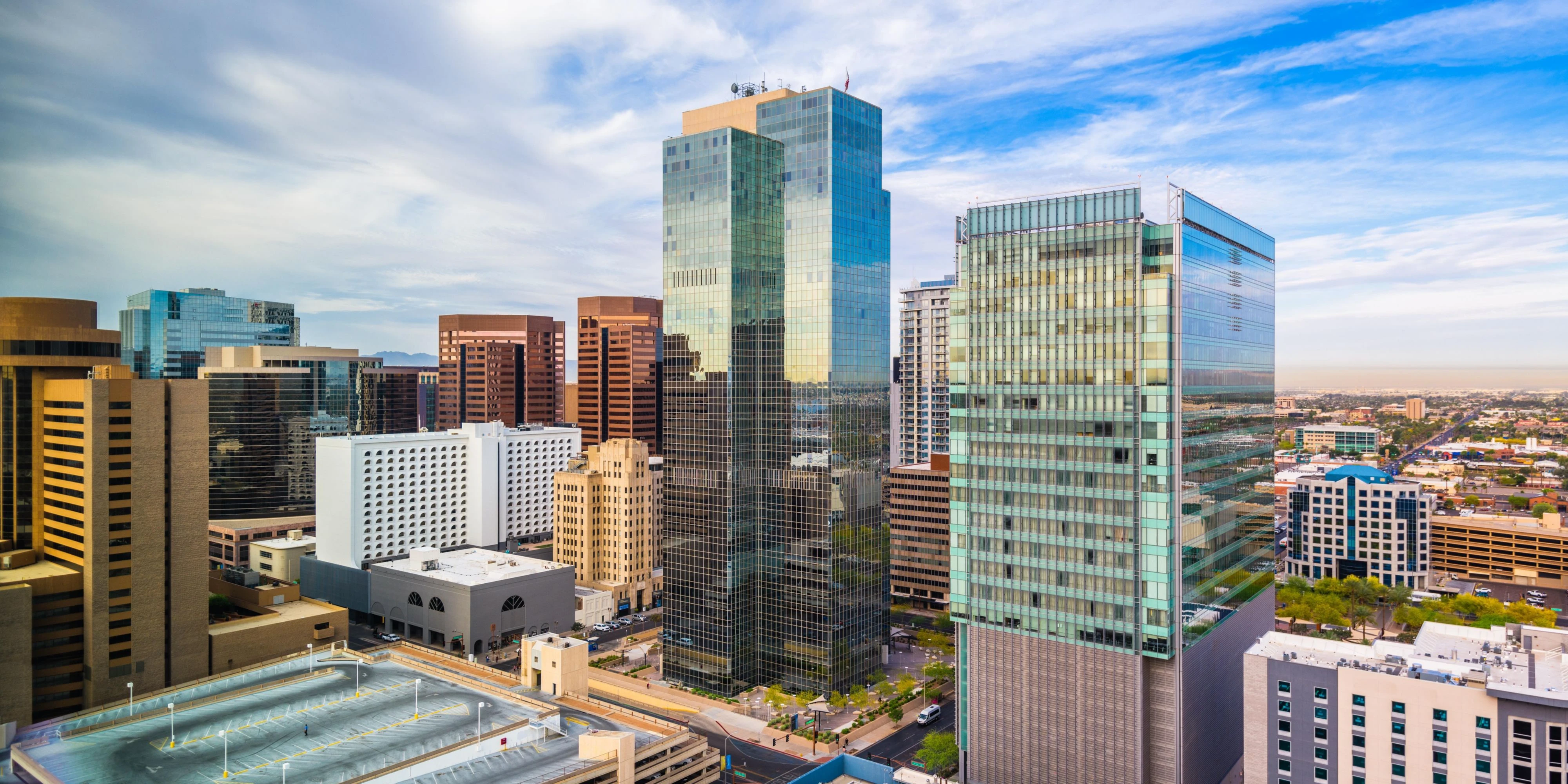Downtown cityscape with modern high-rise buildings under a partly cloudy blue sky.