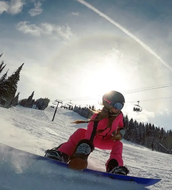 Stylist carving down a sunlit ski run in a bright pink snowsuit and helmet