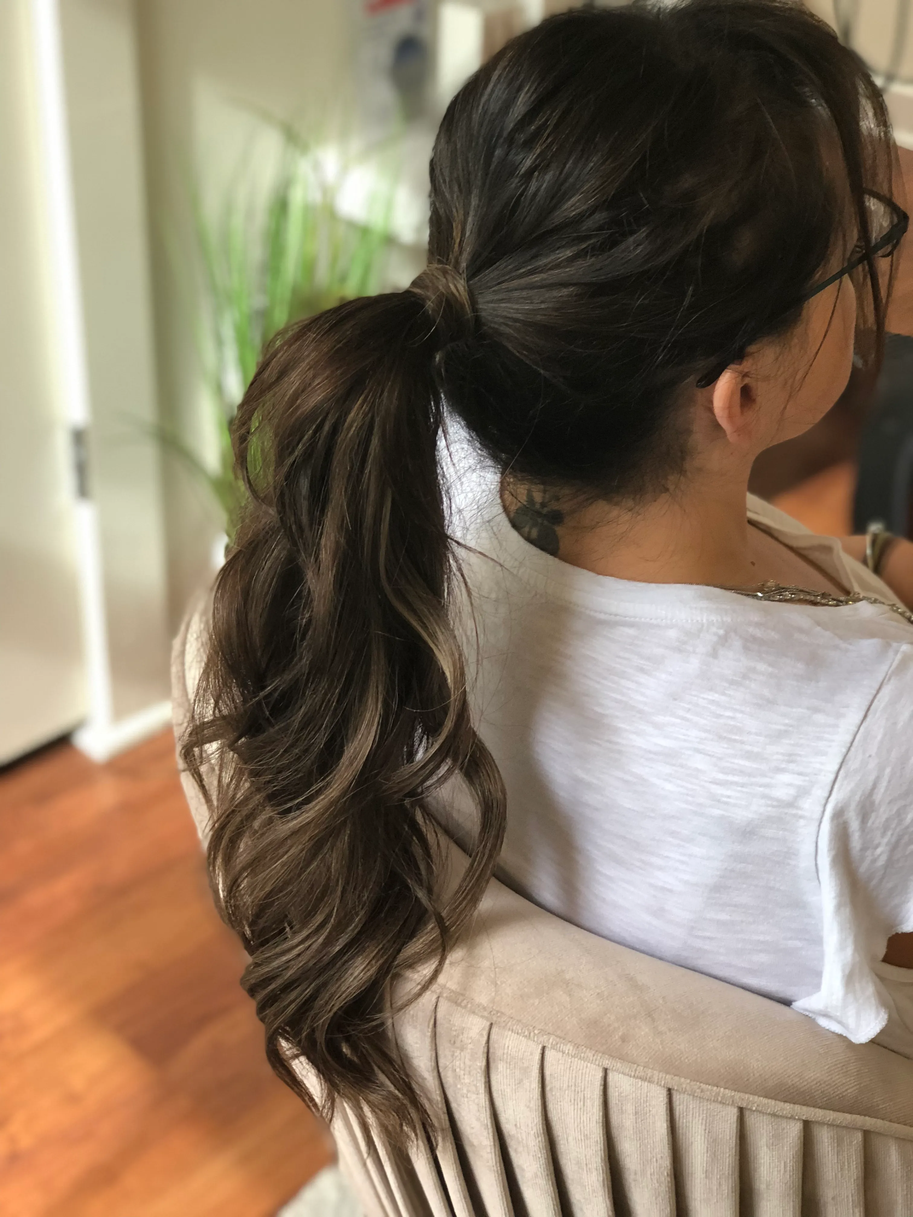 Low brunette ponytail with curled lengths falling over one shoulder