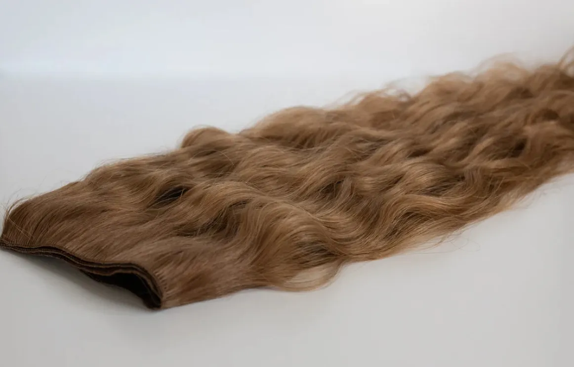 A single hand-tied weft of wavy light brown hair laid flat on white