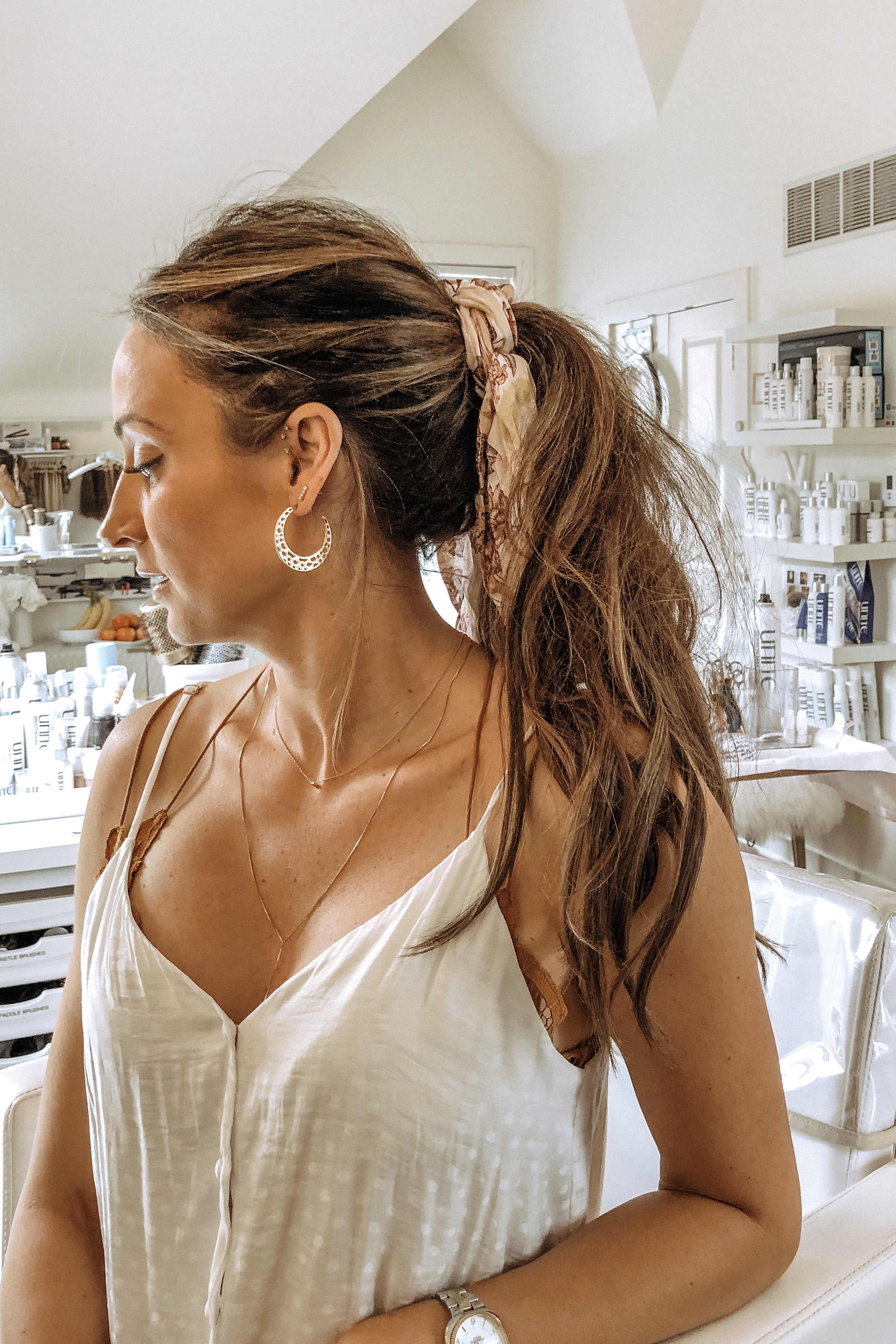 Client with long extensions in a textured ponytail, standing by the salon's product shelves