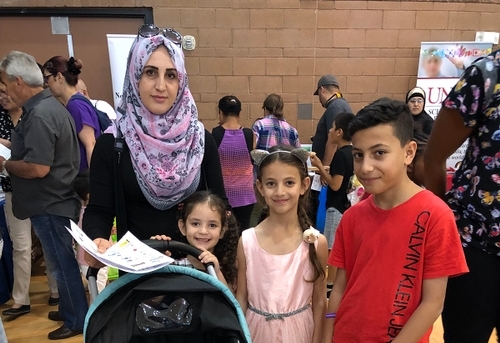 A mother wearing a headscarf standing next to her two daughters and son
