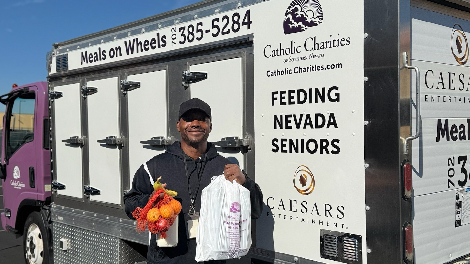 Volunteer standing outside of the Meals on Wheels truck with a door open while holding a bag of food