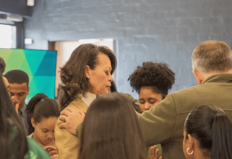 The leaders praying for a woman while the younger generation is surrounding.