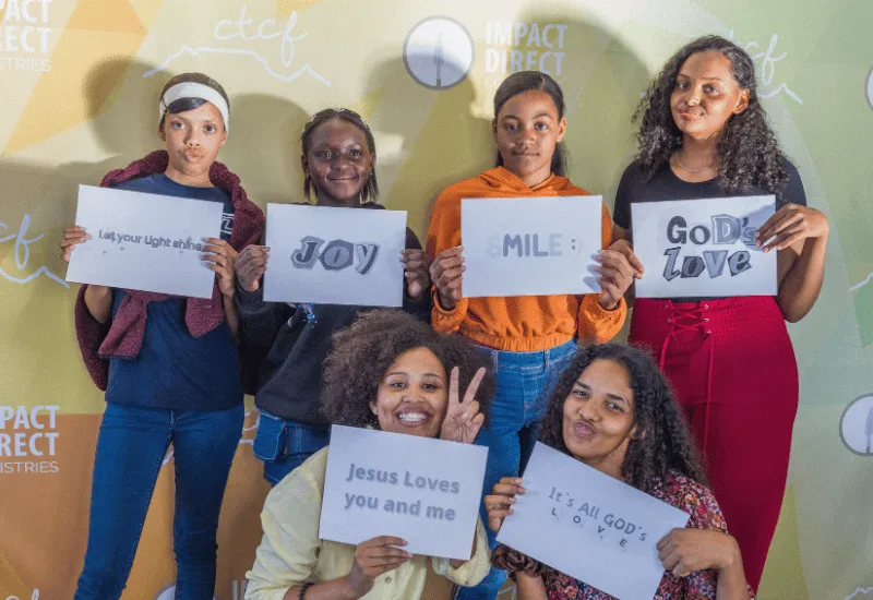 A group of youth posing with various words on a piece of paper.