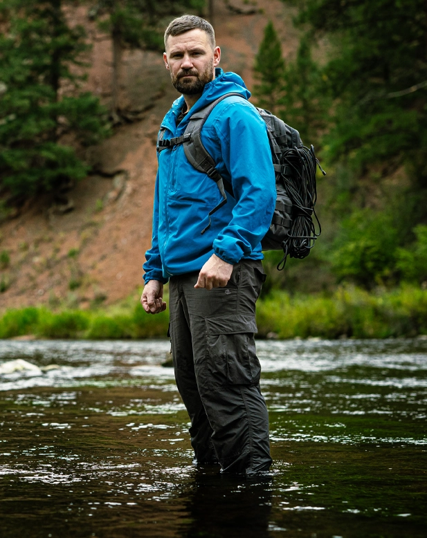 Steven Kelly standing in a river wearing expedition clothing and carrying a rucksack