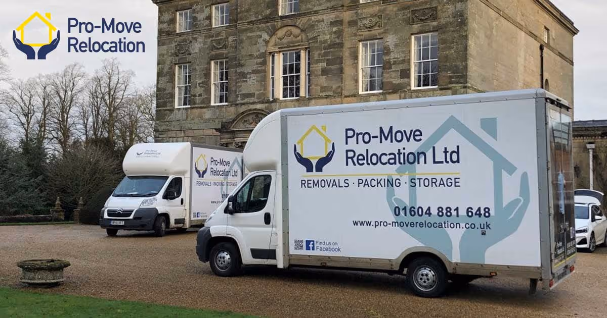 Two moving trucks parked outside a large stone building, displaying the Pro-Move Relocation logo.