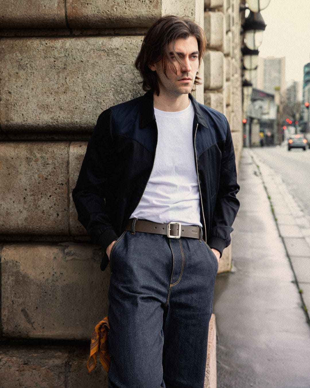 Modern Americana look with dark navy western vest, white tee, raw jeans, hand-burnished leather belt and bandana, in an urban setting