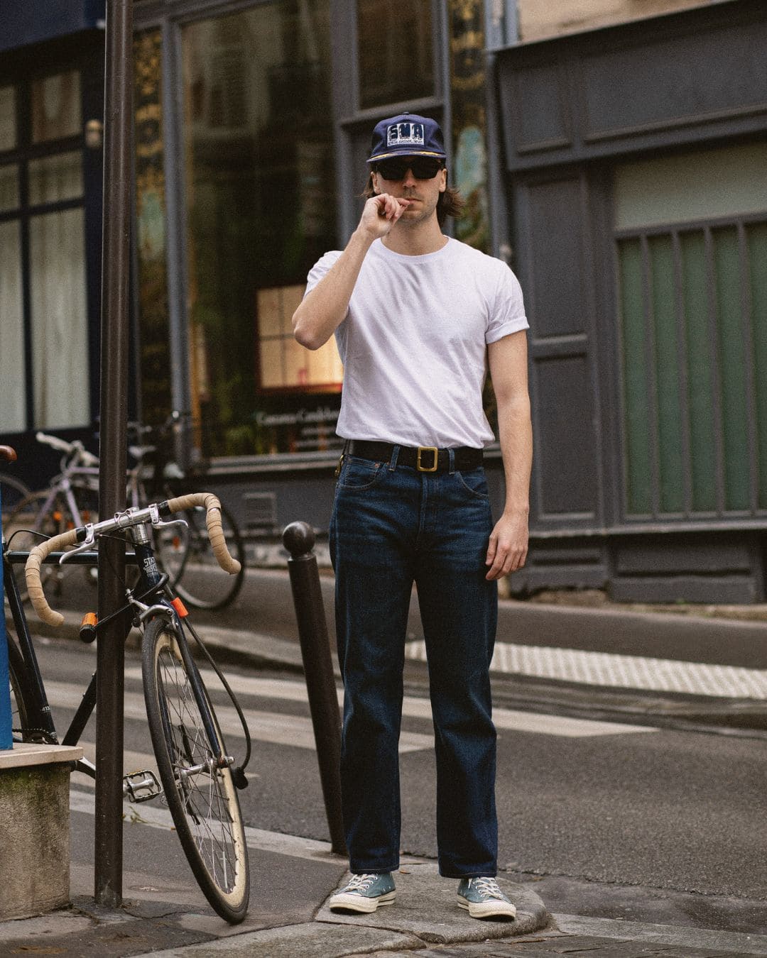 Urban Modern Americana look with white tee, raw jeans and cap, standing in a Paris street with a vintage bicycle