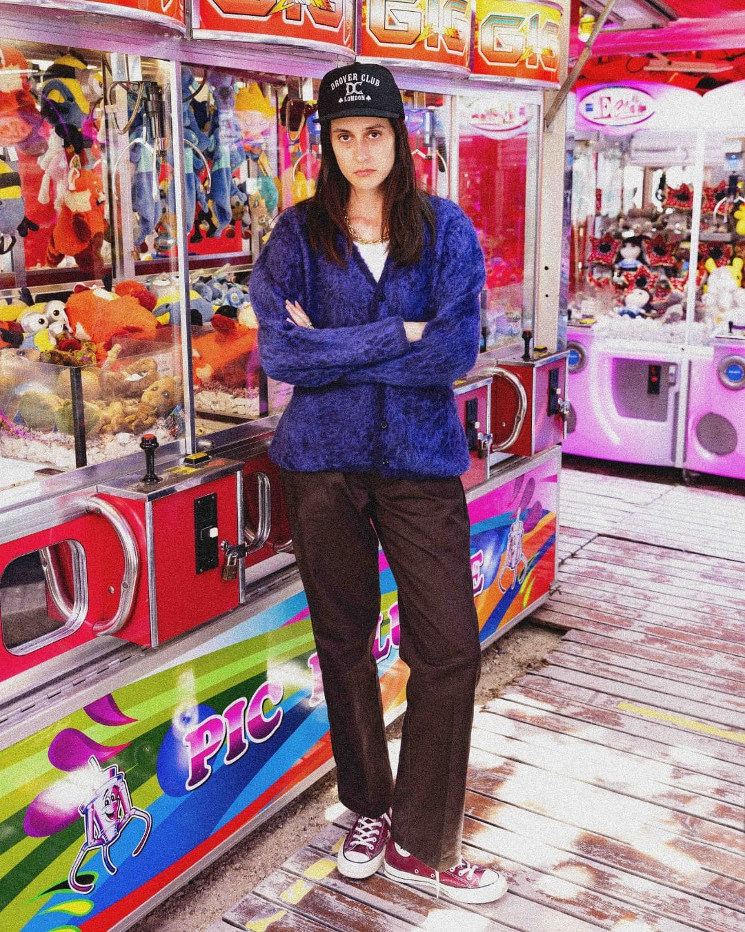 Modern Americana women's look with blue cardigan, black trucker cap and burgundy converse in a vintage fairground