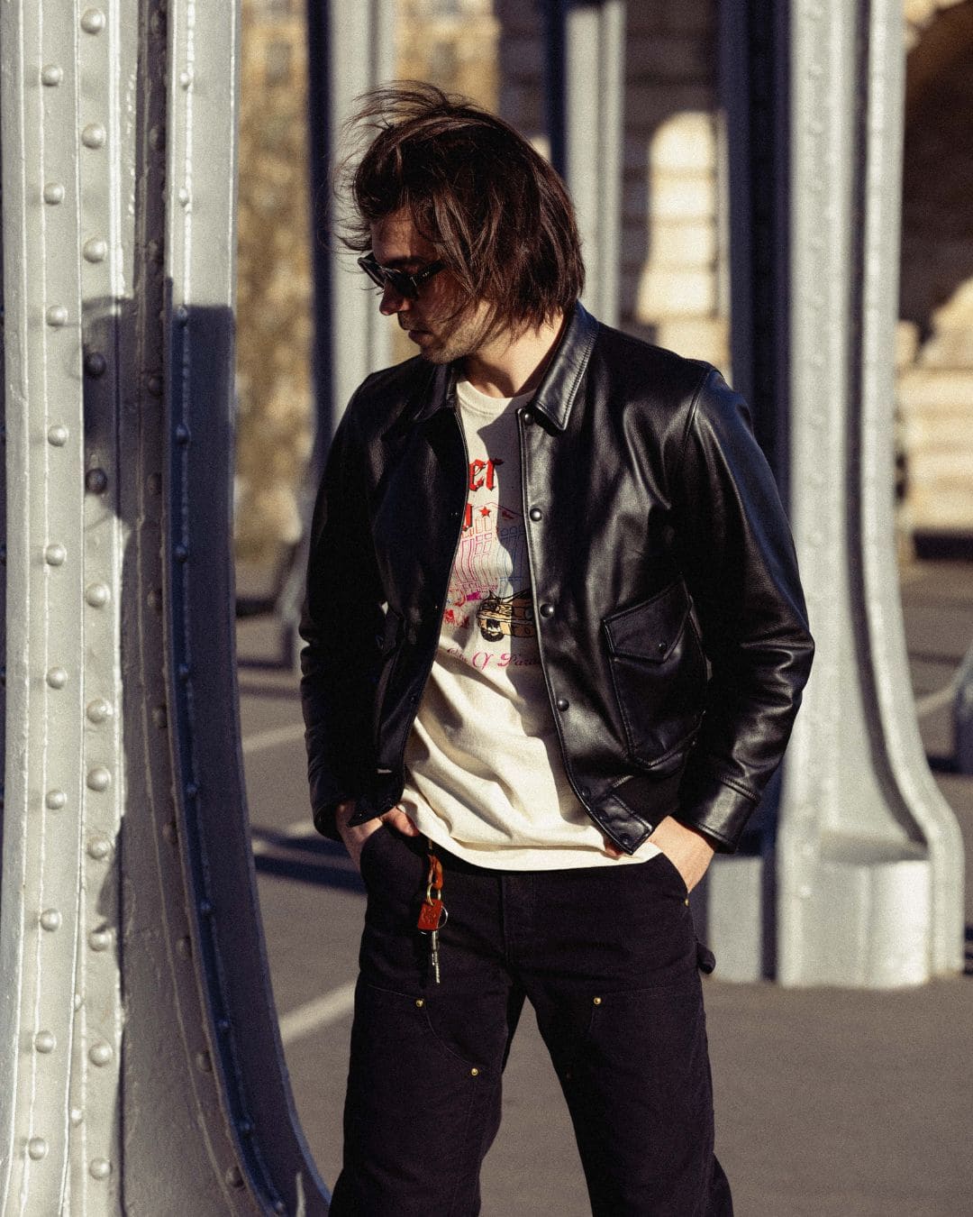 Modern Americana look with black leather jacket and Drover Club graphic tee in an urban metallic structure with golden hour light