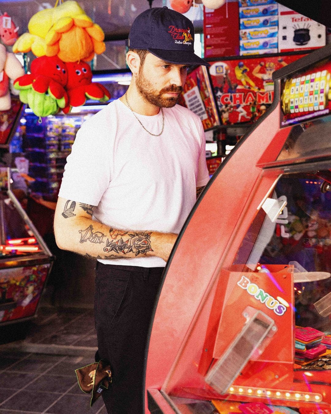Modern Americana look with white tee and Drover Club 5 panel cap in a retro arcade setting