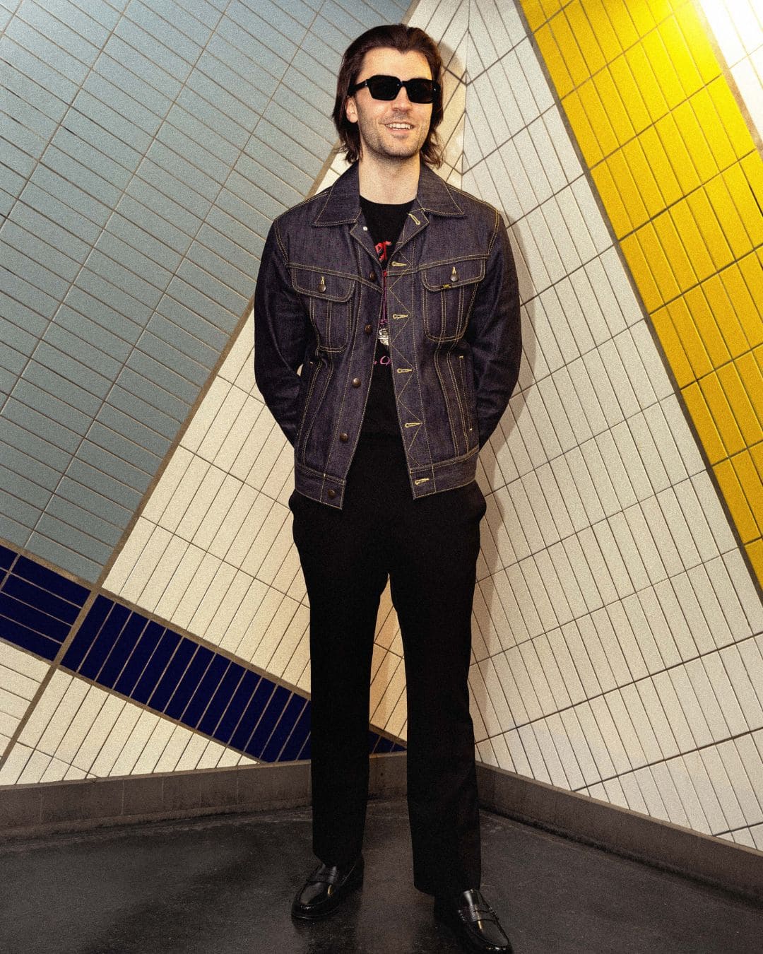 Modern Americana look with raw denim trucker jacket, black tee and tailored pants in a graphic subway-style setting
