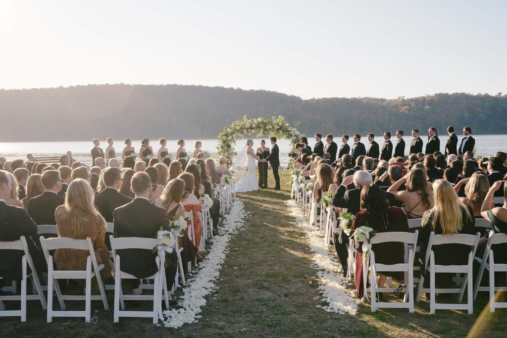 Outdoor wedding ceremony by a lake with guests seated as the couple exchanges vows.