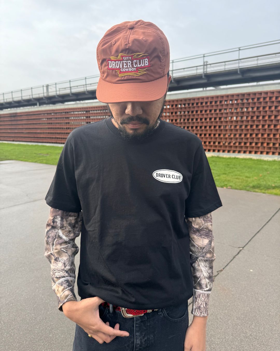 Men's Americana look with brown nylon Blazing Cowboy 5 Panel cap, black Drover Club tee and camo long sleeve layering.