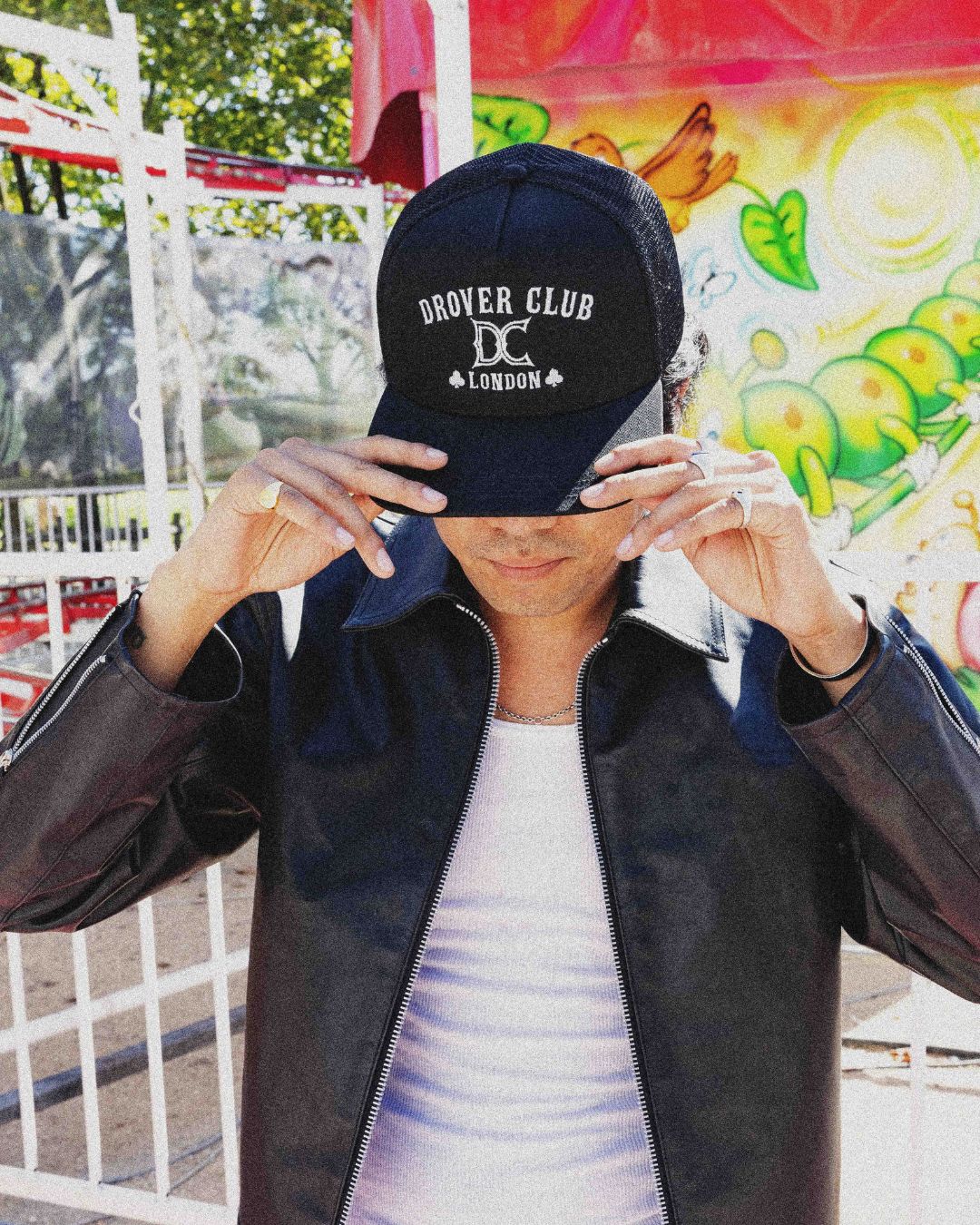 Man wearing a black logo trucker cap and black leather jacket, contemporary Americana look.