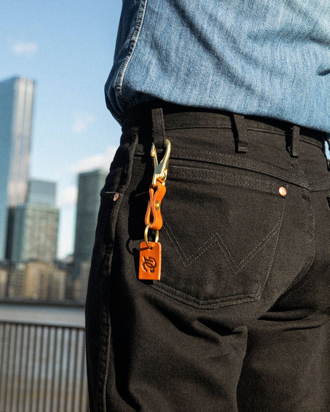 Close-up of the Tan Drover Club leather key clip on black denim jeans, premium leather accessory.