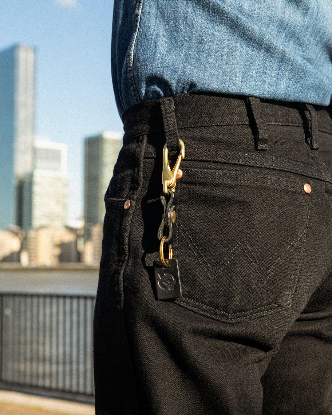 Close-up of the black Drover Club leather key clip attached to black denim jeans, practical and stylish accessory.
