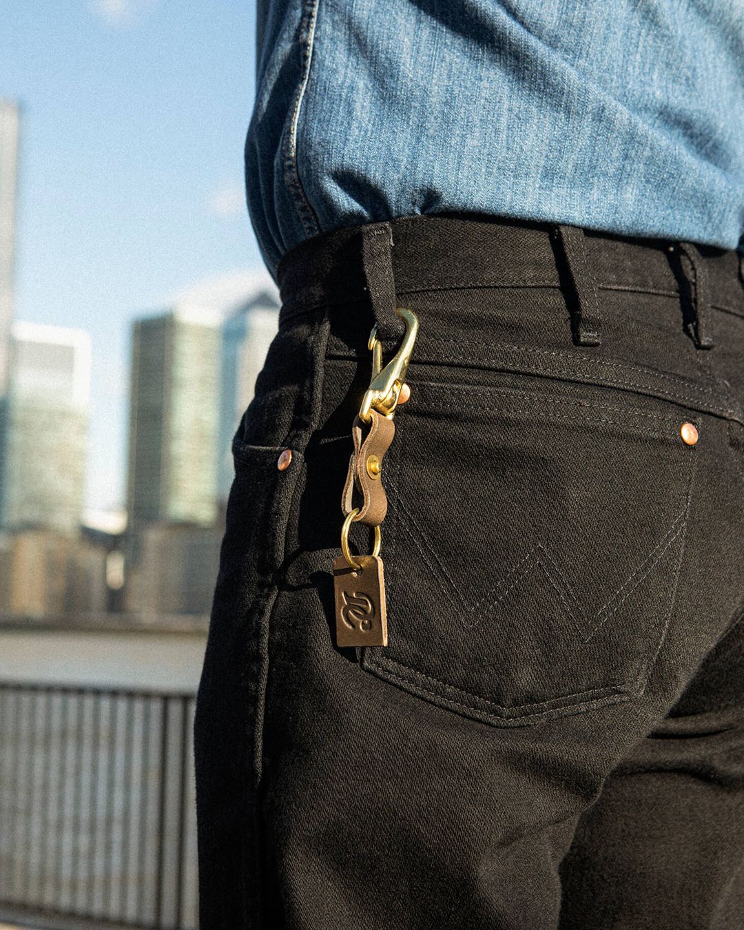 Close-up of the grey Drover Club leather key clip attached to black denim jeans, Americana chic accessory.
