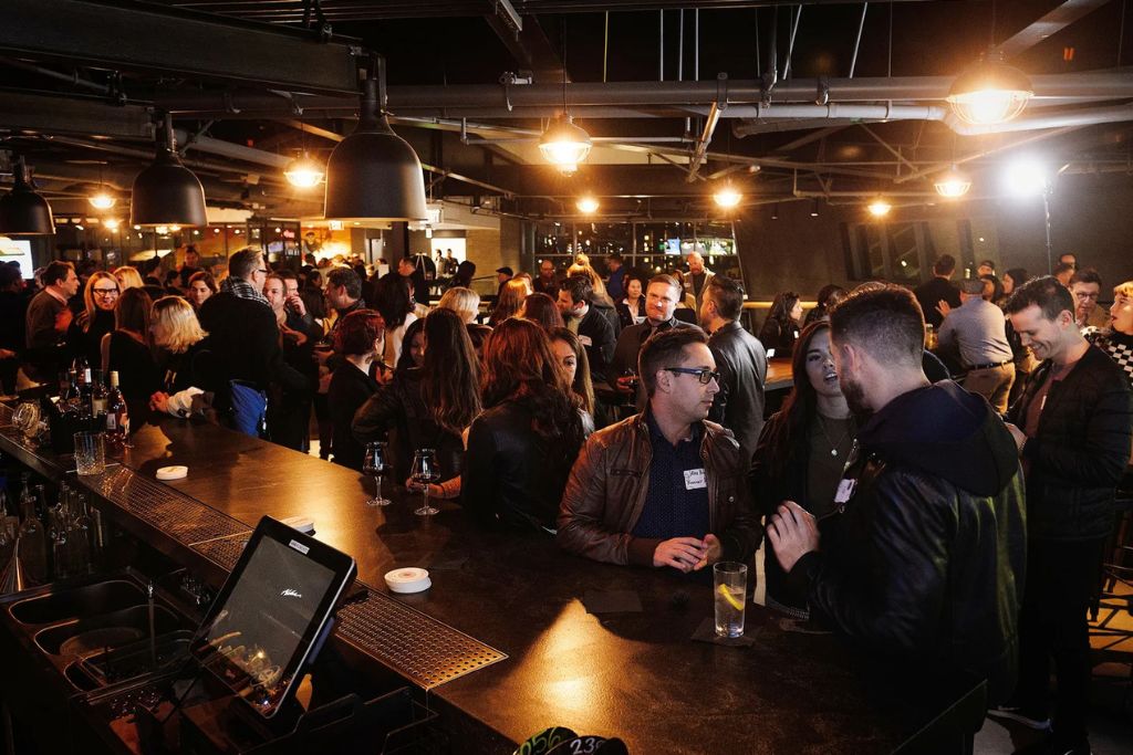 Professionals attending an evening networking event inside a modern bar venue.