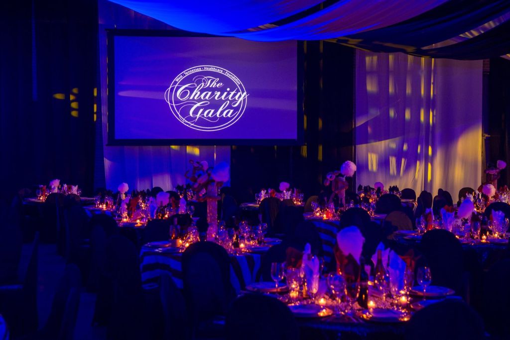 Elegant ballroom prepared for a charity gala with candlelit tables set for a formal black tie evening.